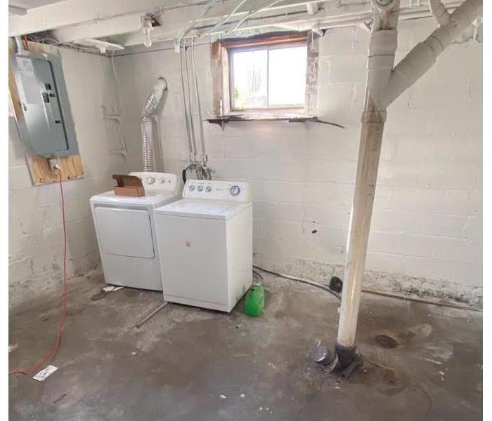 A unfinished basement with just a washer and dryer and white painted walls.