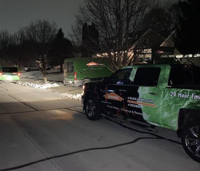 Servpro green trucks in a residential driveway at night.