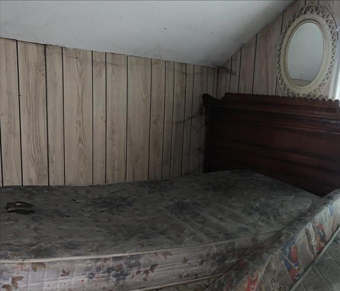 Small bedroom in loft area with wood boards on the wall and soot on the mattress and wall.